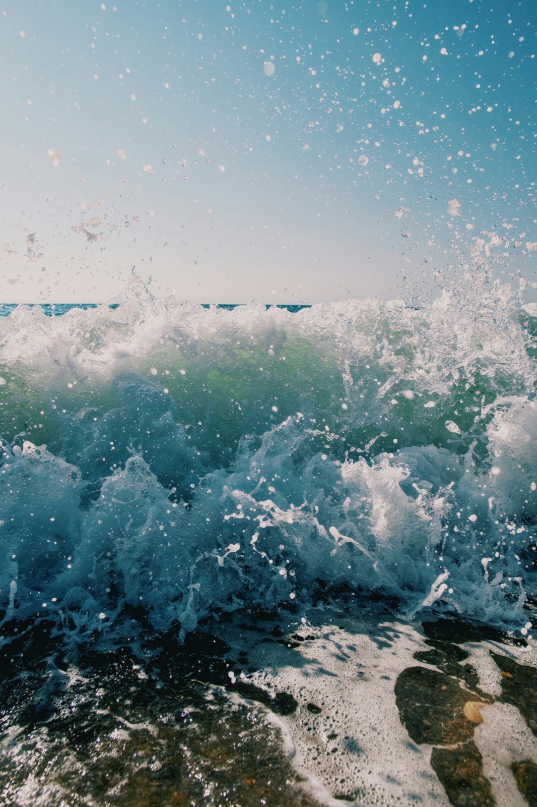 A wave breaking hard against dark rocks, spray bursting upward